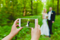 Somebody is using smartphone to make a photo of newlyweds in summer forest